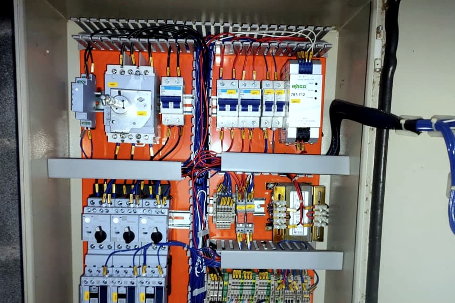 Painel de automação aberto, com contatores, disjuntores, fonte, réguas de bornes e grande densidade de condutores azuis e vermelhos identificados por anilhas.